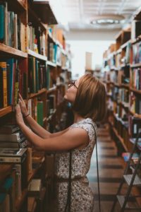 woman searching a full bookshelf for something to read, 5 books by indigenous authors you might not have read yet