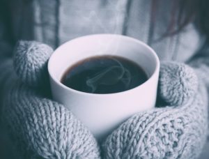 mittened hands hold a mug of coffee